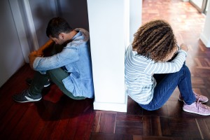 Couple sitting on opposite sides of the wall and feeling sad